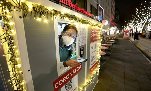 Coronavirus test center employee Denise waits for clients on the famous “Kurfuerstendamm (Ku'damm)” shopping road in Berlin, Germany, Tuesday, December 21, 2021. Germany has announced new restrictions aimed at slowing the spread of the new omicron variant of COVID-19. The new rules, which go into effect on Dec. 28, fall short of a full lockdown but include contact restrictions for vaccinated people. (Photo by Michael Sohn/AP Photo)