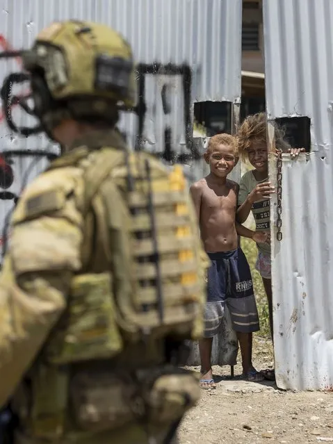 In this photo provided by the Department of Defence, Australian Army Corporal Aaron Woodham is watched by young boys during a community engagement patrol through Honiara, Solomon Islands, Saturday, November 27, 2021. Solomon Islands police have found multiple bodies in a burned-out building and arrested more than 100 people in this week's violence sparked by concerns about the Pacific nation's increasing links with China. (Photo by Cpl. Brandon Grey/Department of Defence via AP Photo)