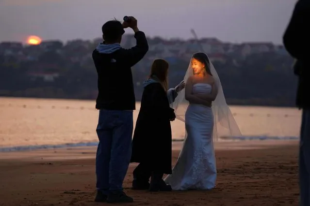 A bride's face is lit up as she gets ready to take wedding photos as the sun sets in Qingdao in eastern China's Shandong province, Sunday, April 21, 2024. (Photo by Ng Han Guan/AP Photo)