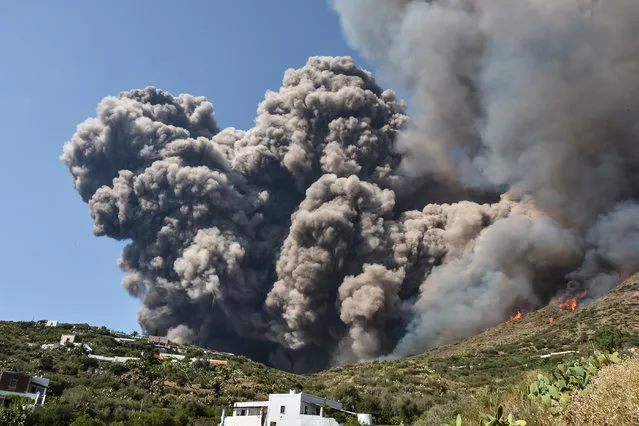 Smoke billows and flames propaqate accross the hillside neqr houses after the Stromboli volcano erupted on July 3, 2019 on the Stromboli island, north of Sicily. A volcano on the Italian island of Stromboli erupted dramatically on July 3, killing a hiker and sending tourists fleeing into the sea. (Photo by Giovanni Isolino/AFP Photo)