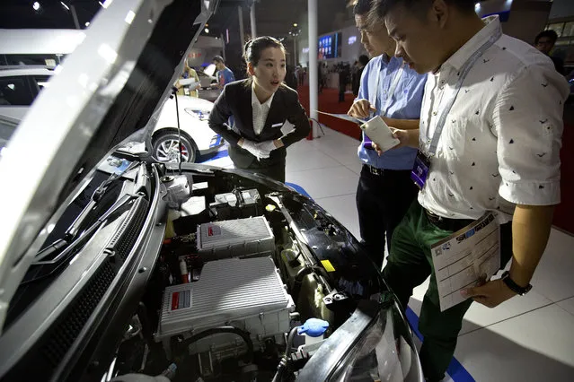 A staff member talks with visitors as they look over the motor of an iEV5 electric car from Chinese automaker JAC on display at the Beijing International Automotive Exhibition in Beijing, Monday, April 25, 2016. (Photo by Mark Schiefelbein/AP Photo)
