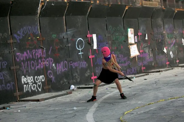 A woman throws debris toward a fence during a protest to mark International Women's Day, in Mexico City, Mexico on March 8, 2022. (Photo by Reuters/Stringer)