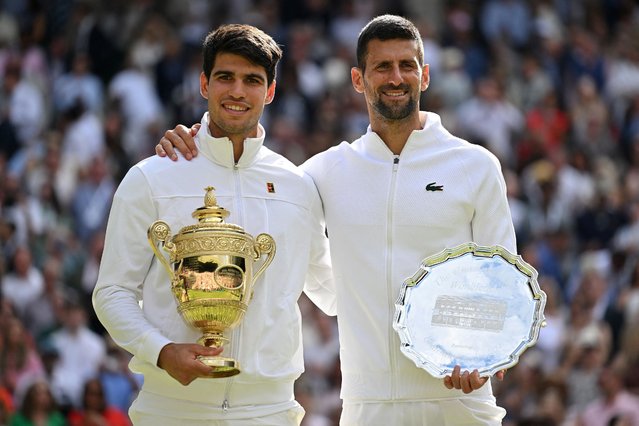 Spain's Carlos Alcaraz holding the winner's trophy (L) and second-placed Serbia's Novak Djokovic pose for pictures during the price ceremony at the end of their men's singles final tennis match on the fourteenth day of the 2024 Wimbledon Championships at The All England Lawn Tennis and Croquet Club in Wimbledon, southwest London, on July 14, 2024. Defending champion Alcaraz beat seven-time winner Novak Djokovic in a blockbuster final, with Alcaraz winning 6-2, 6-2, 7-6. (Photo by Andrej Isakovic/AFP Photo)