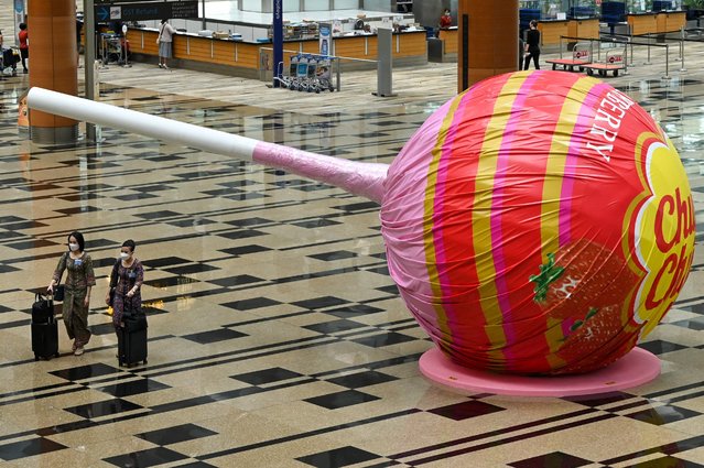 Singapore Airlines stewardesses walk past a giant lollipop candy display at Changi International Airport in Singapore on April 1, 2022, as Singapore reopened its land and air borders to travellers fully vaccinated against the Covid-19 coronavirus. (Photo by Roslan Rahman/AFP Photo)