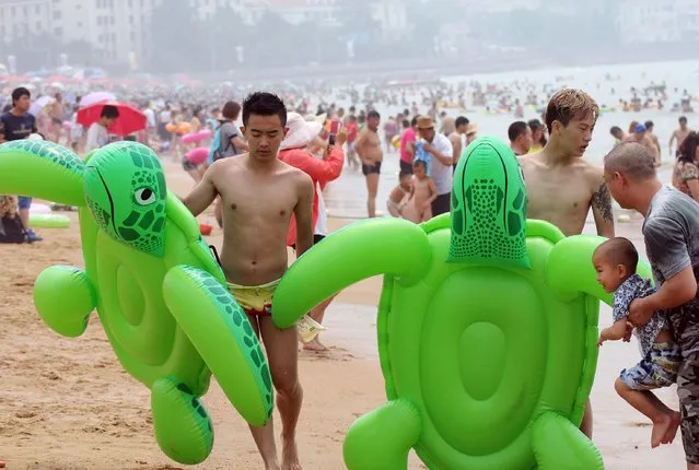 This picture taken on July 13, 2015 shows beachgoers with inflatable turtles amid high temperature on a beach in Qingdao, east China's Shandong province. (Photo by AFP Photo)