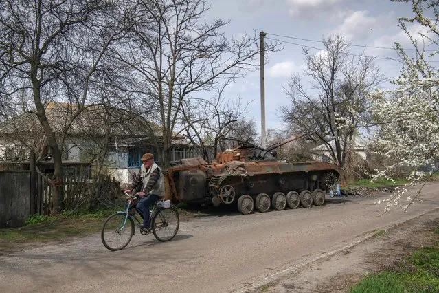A man rides a bicycle past the debris of Russian military machinery destroyed during Russia's invasion of Ukraine in the village of Rusaniv, Kyiv region, Ukraine on April 25, 2022. (Photo by Vladyslav Musiienko/Reuters)