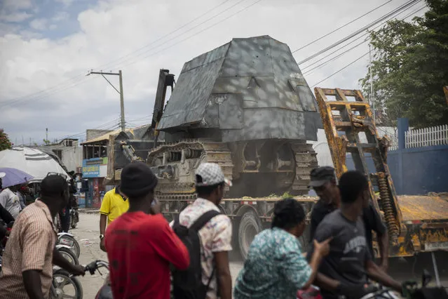 Residents watch as an armored police car is transported on the bed of trailer, to be used in an anti-gang operation in Croix-des-Missions, north of Port-au-Prince, Haiti, Thursday, April 28, 2022. (Photo by Joseph Odelyn/AP Photo)