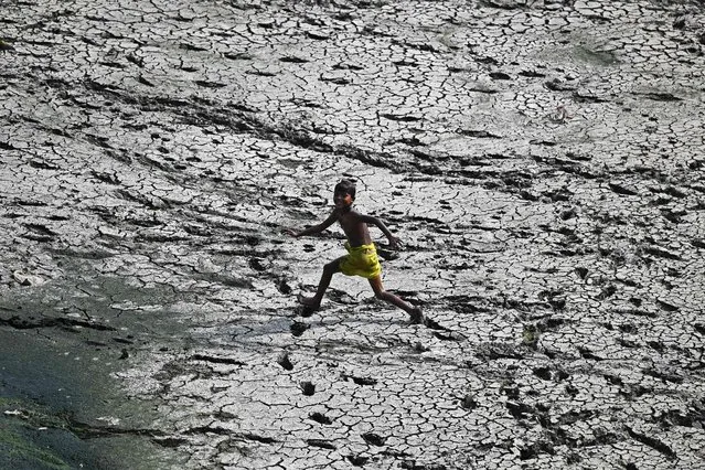 A boy runs across a patch of parched riverbed of Yamuna on a hot summer day in New Delhi on May 2, 2022. (Photo by Sajjad Hussain/AFP Photo)