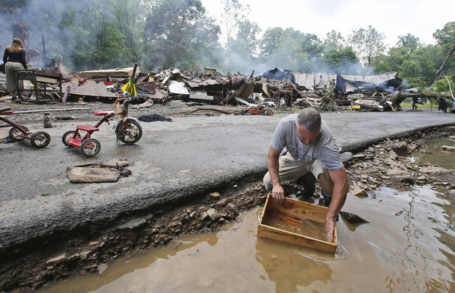 Mark Lester cleans out a box with creek water as he cleans up from severe flooding in White Sulphur Springs, W. Va., Friday, June 24, 2016. (Photo by Steve Helber/AP Photo)