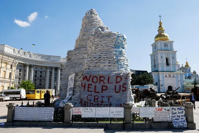 Pedestrians walk past banners reading “World – Help us” on sand bags which are covering and protecting the Monument to Princess Olga, St. Andrew the Apostle and the educators Cyril and Methodius during a trip of French President, German Chancellor and Italian Prime Minister in Kyiv, Ukraine, June 16, 2022. (Photo by Ludovic Marin/Pool via Reuters)