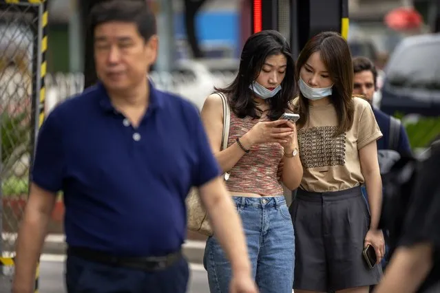Women wearing face masks look at a smartphone as they stand on a street corner in Beijing, Wednesday, July 6, 2022. (Photo by Mark Schiefelbein/AP Photo)