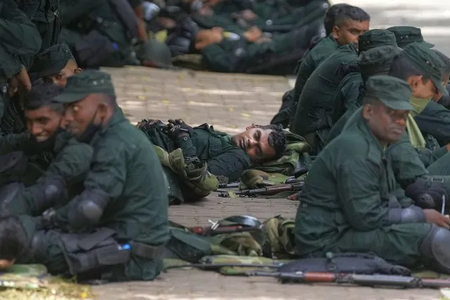 Army soldiers rest on the sidewalk of a barricaded road that leads to the parliament in Colombo, Sri Lanka, Thursday, July 14, 2022. Sri Lankan protesters began to retreat from government buildings they had seized and military troops reinforced security at the Parliament on Thursday, establishing a tenuous calm in a country in both economic meltdown and political limbo. (Photo by Eranga Jayawardena/AP Photo)