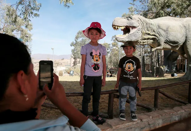 A mother takes a photograph of her children while they pose in front of the replica of a Tyrannosaurus rex at the Cretaceous park in Cal Orcko, on the outskirts of Sucre, Bolivia, July 22, 2016. (Photo by David Mercado/Reuters)