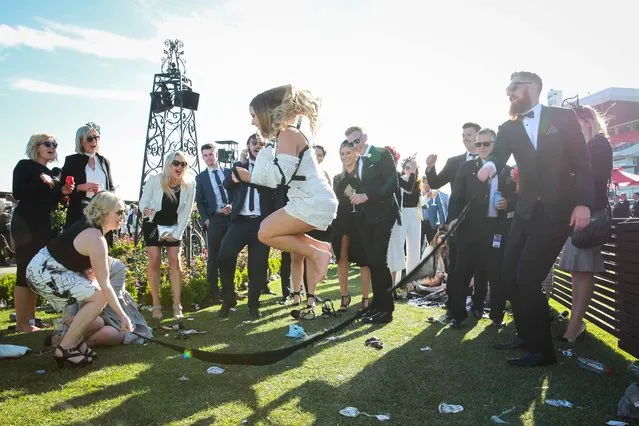 A woman leaps in the air and two pals swing a makeshift skipping rope on 2017 Derby Day at Flemington Racecourse on November 4, 2017 in Melbourne, Australia. (Photo by Splash News and Pictures)