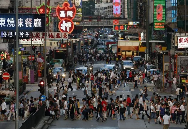 In this September 10, 2014, photo, pedestrians cross the road in the Hong Kong shopping district of Mongkok during rush hour. On packed subways and crowded streets, billions of people worldwide participate in a short-distance population shift twice a day: the rhythmic ritual of the daily commute to and from work. (Photo by Kin Cheung/AP Photo)