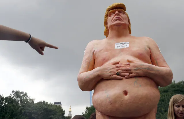A woman points at a statue of a naked Republican presidential candidate Donald Trump, Thursday, August 18, 2016 in New York's Union Square. The statue was removed by New York City Department of Parks & Recreation employees. (Photo by Mary Altaffer/AP Photo)
