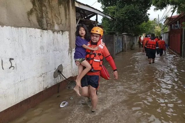 In this photo provided by the Philippine Coast Guard, a rescuer carries a girl over flood waters caused by Tropical Storm Nalgae in Zamboanga, southern Philippines on Saturday October 29, 2022. Flash floods and landslides set off by torrential rains left dozens of people dead, including in a hard-hit southern Philippine province, where many villagers are feared missing and buried in a deluge of rainwater, mud, rocks and trees, officials said Saturday. (Photo by Philippine Coast Guard via AP Photo)
