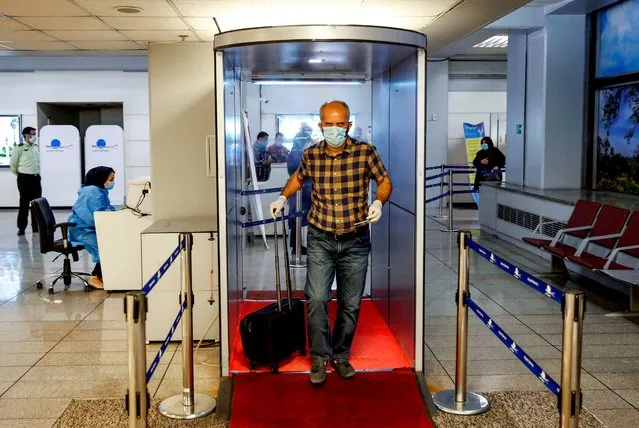 An incoming passenger crosses with his luggage through a disinfection tunnel upon arriving on an Emirates flight at the Iranian capital Tehran's Imam Khomeini International Airport on July 17, 2020. The UAE's Emirates airlines landed its first flight in Tehran on July 17 after a six month shutdown due to the novel coronavirus pandemic. (Photo by AFP Photo/Stringer)