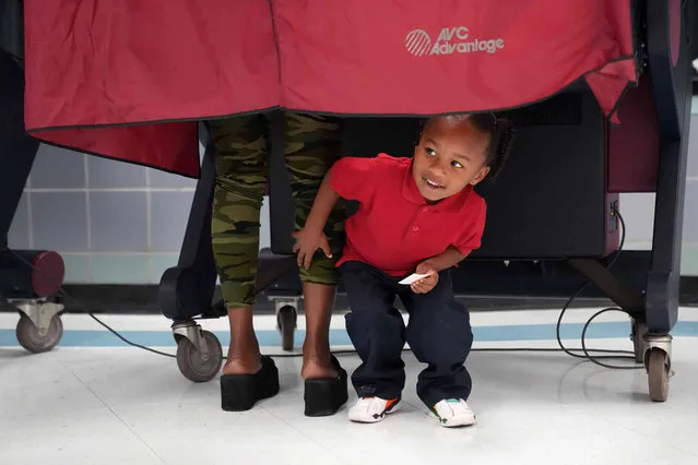 Kash Strong, 3, peeks out from under the curtain of a voting booth as his mother Sophia Amacker casts her vote on Election Day at the Martin Luther King Elementary School in the Lower Ninth Ward of New Orleans, Tuesday, November 8, 2022. (Photo by Gerald Herbert/AP Photo)