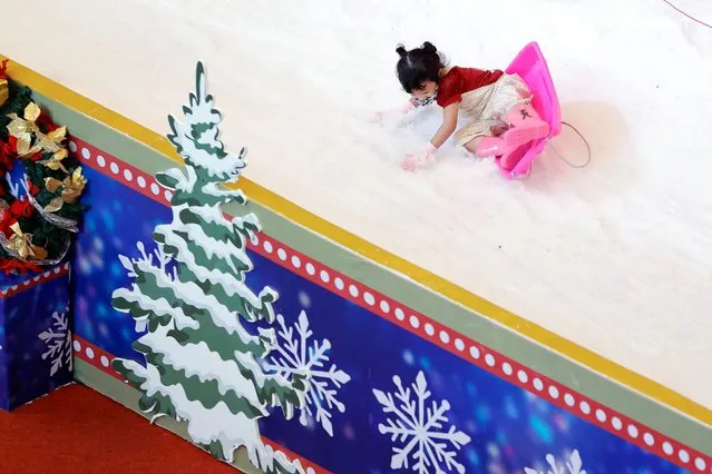 A girl falls from a sledge as she slides on artificial snow while playing at a playground inside the Taman Anggrek shopping mall, during the Christmas and New Year season in Jakarta, Indonesia on December 15, 2022. (Photo by Willy Kurniawan/Reuters)