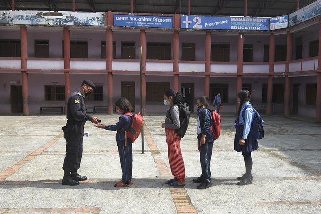 A security guard gives hand sanitiser to students as they arrive at the Prabhat secondary school as some schools reopened after a six-month closure due to the Covid-19 coronavirus pandemic in Chandagiri municipality on the outskirts of Kathmandu on October 6, 2020. (Photo by Prakash Mathema/AFP Photo)