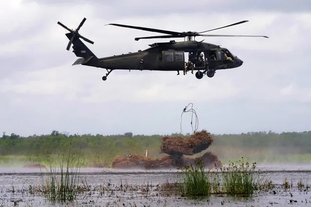 A Louisiana National Guard helicopter crew drops a bundle of Christmas trees into the marsh, as barrier protection to the shoreline, in the Bayou Sauvage Urban National Wildlife Refuge in New Orleans, Wednesday, April 26, 2023. (Photo by Gerald Herbert/AP Photo)