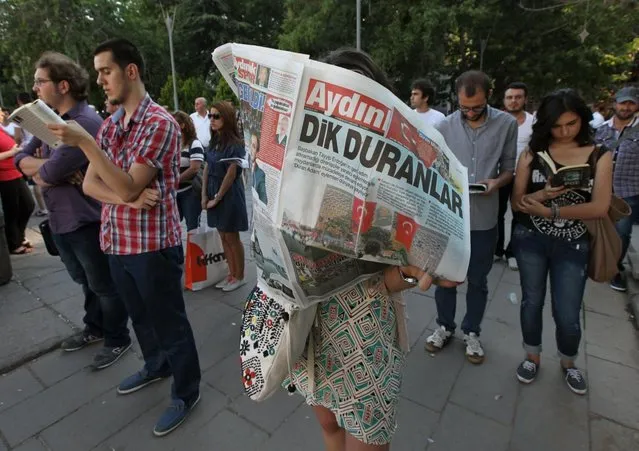 A woman reads a newspaper with the headline reading “Standing men”, during a silent protest in Guven Park in Ankara, Turkey, Wednesday, June 19, 2013. After weeks of sometimes-violent confrontation with police, Turkish protesters have found a new form of resistance, standing still and silent. (Photo by Burhan Ozbilic/AP Photo)