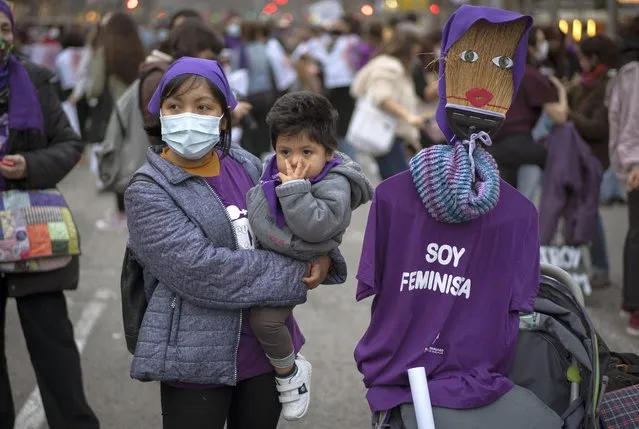 A woman holds her son during a gathering celebrating International Women's Day in Barcelona, Spain, Monday, March 8, 2021. Women in Spain are marking this year's International Women's Day with static protests, bicycle fun-rides and small-sized events to prevent gatherings that could trigger a new spike of coronavirus infections. (Photo by Emilio Morenatti/AP Photo)