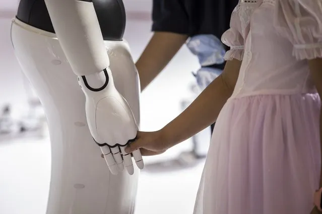 A child holds the hand of a Leju Robotics Co. humanoid robot at the World AI Conference (WAIC) in Shanghai, China, on Friday, July 7, 2023. Chinese artificial intelligence-related stocks, including Cambricon Technologies and Iflytek, gain as a two-day conference centering on China's AI effort backed by influential regulatory agencies kicked off in Shanghai. (Photo by Qilai Shen/Bloomberg)