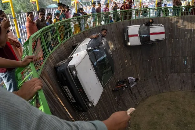 Ravi Kumar stretches out his hand from his fast moving car to receive a currency note offered by a spectator in an enclosure known as Maut ka Kuan, or the well of death, at a local fair in Dharmsala, India, Saturday, April 9, 2022. Ravi and others perform death defying stunts for very little money at traditional fairs all over the country. (Photo by Ashwini Bhatia/AP Photo)