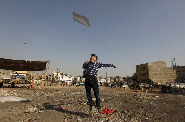Eight-year-old Aayan helps his friend to fly a kite along a littered ground near a low income residential area in Karachi, Pakistan, December 20, 2015. (Photo by Akhtar Soomro/Reuters)