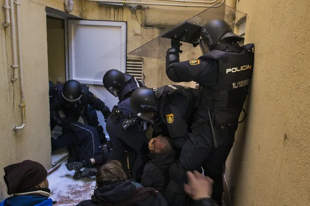 Riot police grab the face of an activist as they remove housing right activists who tried to stop Umberto Jimenez's eviction in Madrid, Spain, Monday, February 9, 2015. Umberto Jimenez, 46 years old, lost his foreclosed apartment to a moneylender after he could not afford to pay his debt due to his financial situation. (Photo by Andres Kudacki/AP Photo)