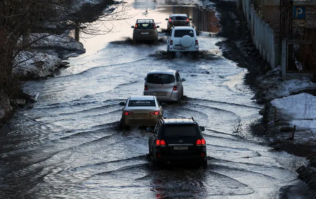 Vehicles drive along a flooded street. The flooding is caused by snowmelt in Omsk, Russia on April 6, 2021. (Photo by Yevgeny Sofiychuk/TASS)