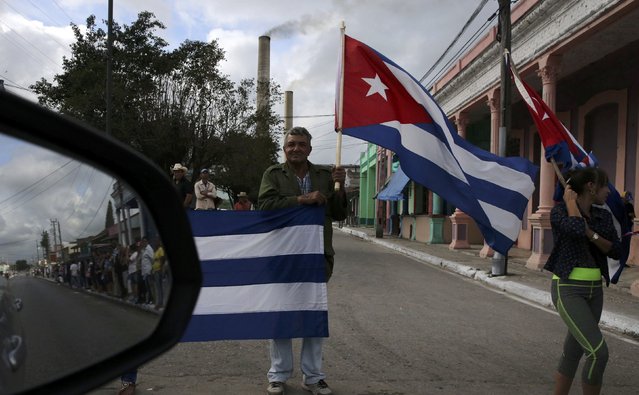People carry Cuban flags as they and others reflected in a mirror await the caravan carrying Fidel Castro's ashes in Jatibonico, Cuba, December 1, 2016. (Photo by Carlos Barria/Reuters)