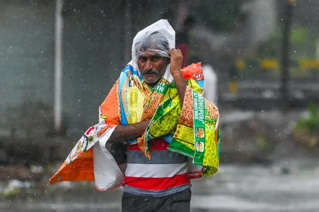 A man covers himself with plastics as he walks along a street in Amreli on May 18, 2021, after Cyclone Tautae hit the west coast of India with powerful winds and driving rain, leaving at least 20 people dead. (Photo by Punit Paranjpe/AFP Photo)