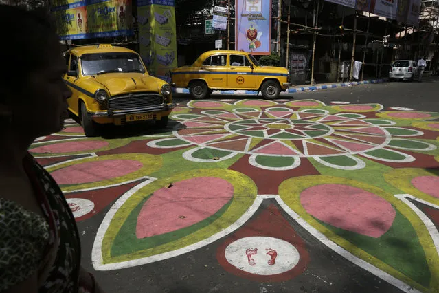 In this October 9, 2018, photo, an Indian woman, left and two yellow cabs prepare to cross an intersection of a street painted with colors ahead of Hindu festival Durga Puja in Kolkata, India. The festival is scheduled to run from Oct. 16 to Oct. 19. (Photo by Bikas Das/AP Photo)
