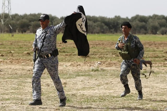 A member of Iraqi security forces run as another holds an Islamist State flag, which they pulled down in the town of al-Alam March 9, 2015. (Photo by Thaier Al-Sudani/Reuters)