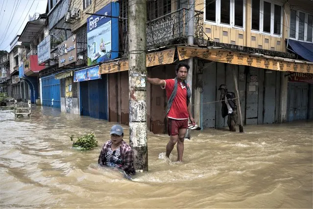 A woman sits next to a man along a flooded street following monsoon rains in Bago township, Bago region, on August 11, 2023. Floods and landslides caused by monsoon rains have killed five people and forced the evacuation of around 40,000 others in Myanmar, officials said on August 11. (Photo by Sai Aung Main/AFP Photo)