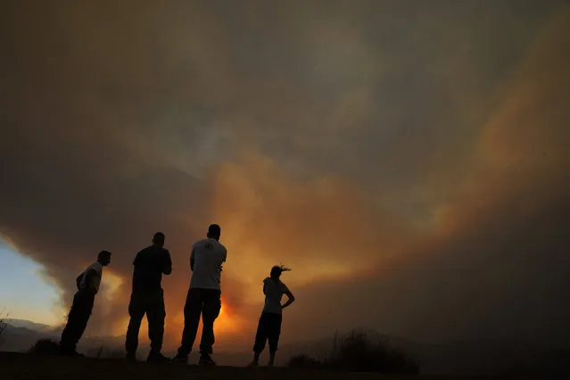 Residents of villages watch a fire in the Larnaca mountain region on Saturday, July 3, 2021. Cyprus has asked fellow European Union member states on Saturday to help battle a huge fire in a mountainous region of the east Mediterranean island nation that has forced the evacuation of at least three villages. (Photo by Petros Karadjias/AP Photo)