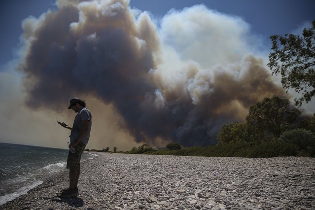 A man checks his mobile phone as an advancing fire engulfs the beach in Cokertme village, in Bodrum, Mugla, Turkey, Monday, August 2, 2021. (Photo by Emre Tazegul/AP Photo)