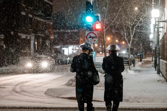 People cross a street in the Mile End, a borough in Montreal, Quebec, Canada, as the snow comes down on December 22, 2022. A “once-in-a-generation” winter storm with temperatures as low as -40 degrees Fahrenheit caused Christmas travel chaos in the United States on Thursday, with thousands of flights cancelled and major highways closed. (Photo by Andrej Ivanov/AFP Photo)