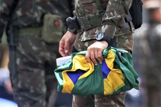 A soldier carefully collects national flags after supporters of former Brazilian former President Jair Bolsonaro left the encampment set up outside army headquarters in Brasilia, Brazil, Monday, January 9, 2023, the day after Bolsonaro supporters stormed government buildings in the capital. (Photo by Gustavo Moreno/AP Photo)