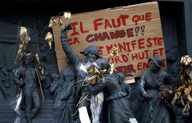 A placard reading “It Has To Change, Demonstrate Today and Vote...” is seen on a statue as activists from left-wing parties and other groups attend a demonstration at the Place de la Republique against corruption in politics, amid a presidential campaign clouded by a fake jobs investigation and other legal scandals, in Paris, Saturday, February 19, 2017. Protesters especially targeted conservative presidential candidate Francois Fillon, under investigation for alleged high-paying but fake parliamentary jobs for his wife and children. (Photo by Francois Mori/AP Photo)