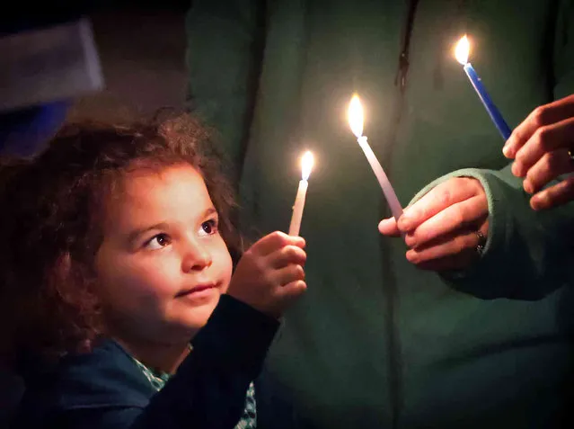 Four-year-old Riley Gillet, of Orlando, lights a candle with her family, marking the beginning of the traditional Jewish holiday of Hanukkah, during the Chabad of Greater Orlando's “Chanukah on the Park” celebration in Winter Park, Fla., late Sunday, November 28, 2021. Held at Central Park, the event included the lighting of a giant menorah, live performers, music and dancing. Jews worldwide will celebrate Hanukkah through Dec. 6. (Photo by Joe Burbank/Orlando Sentinel via AP Photo)