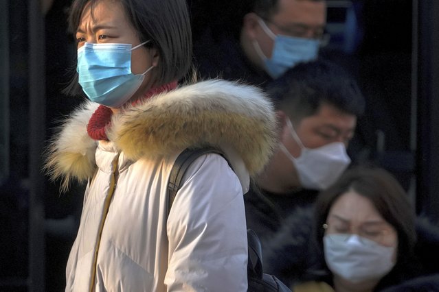 A woman wearing a face mask to protect from the coronavirus walks by masked commuters getting out of a bus during the morning rush hour in Beijing, Monday, January 10, 2022. Tianjin, a major Chinese city near Beijing has placed its 14 million residents on partial lockdown after a number of children and adults tested positive for COVID-19, including at least two with the omicron variant. (Photo by Andy Wong/AP Photo)