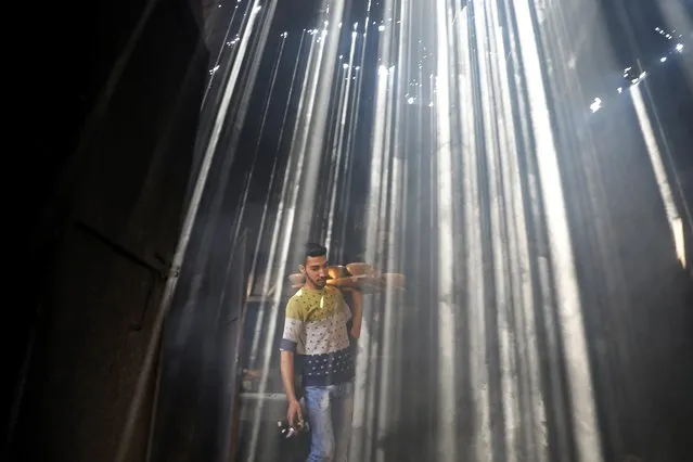 A Palestinian worker carries clay pots as the sun rays penetrate through the ceiling of a pottery workshop in Gaza City on June 11, 2019. (Photo by Mohammed Salem /Reuters)