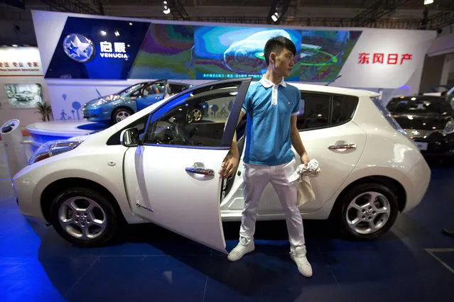 A staff member climbs out of a Morning Wind electric car from Chinese automaker Venucia on display at the Beijing International Automotive Exhibition in Beijing, Monday, April 25, 2016. (Photo by Mark Schiefelbein/AP Photo)
