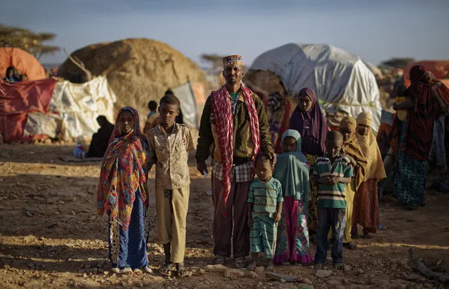 In this photo taken Thursday, March 9, 2017, Ali Hussein, center, and his children who fled the drought stand to be filmed by a television camera in front of their makeshift hut in a camp for the displaced in Qardho in Somalia's semiautonomous northeastern state of Puntland. (Photo by Ben Curtis/AP Photo)