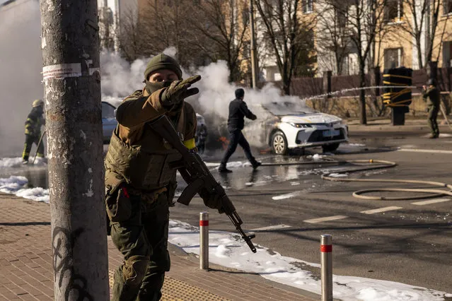 Ukrainian soldiers take positions outside a military facility as two cars burn, in a street in Kyiv, Ukraine, Saturday, February 26, 2022. (Photo by Emilio Morenatti/AP Photo)