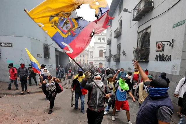 A protester waves a desecrated national flag during a march against President Lenin Moreno and his economic policies during a nationwide strike in Quito, Ecuador, Wednesday, October 9, 2019. Ecuador's military has warned people who plan to participate in a national strike over fuel price hikes to avoid acts of violence. The military says it will enforce the law during the planned strike Wednesday, following days of unrest that led Moreno to move government operations from Quito to the port of Guayaquil. (Photo by Carlos Noriega/AP Photo)